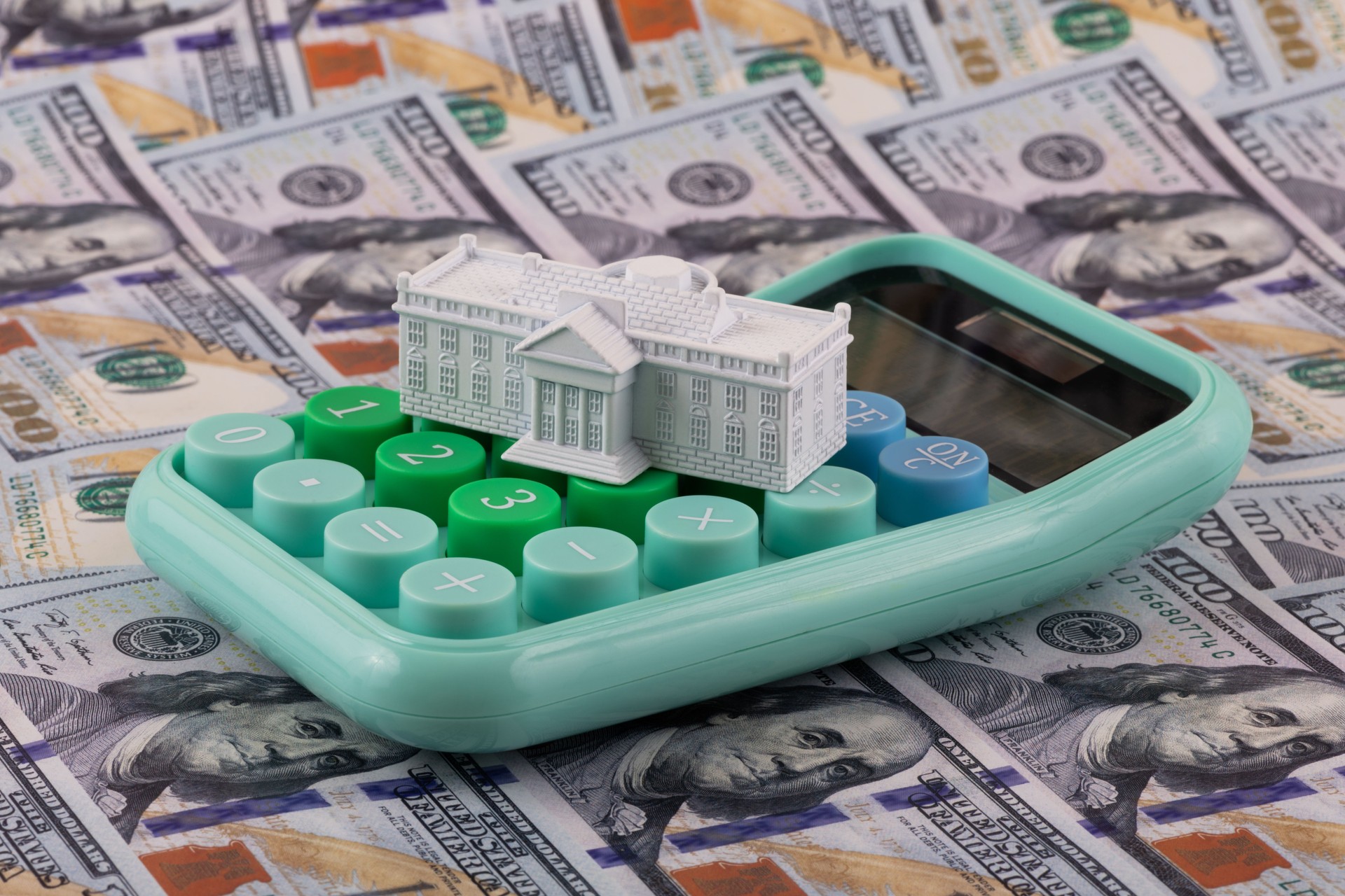 A miniature residence of the President of the United States, the White House, against the backdrop of 100 US dollar bills.